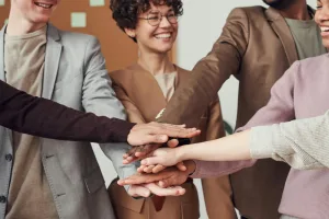 A group of happy, diverse colleagues celebrating teamwork and cooperation with a group high five indoors.